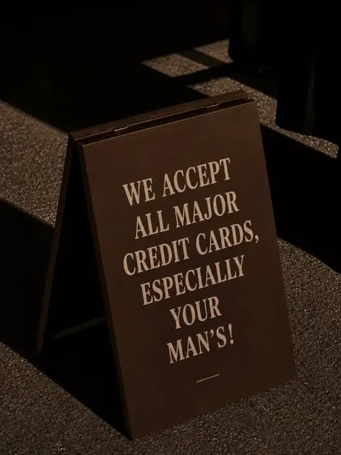Sign reading We accept all major credit cards, especially your man's